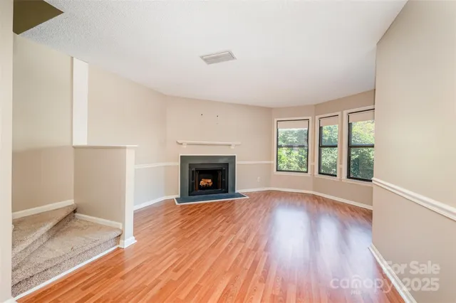 an empty room with wooden floor fireplace and windows