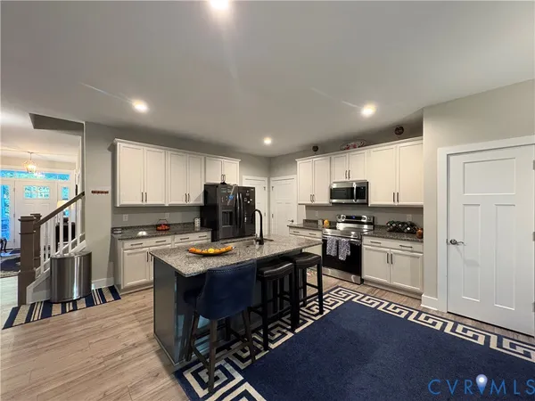 a kitchen with stainless steel appliances kitchen island granite countertop a refrigerator oven a sink a stove and a dining table with wooden floor