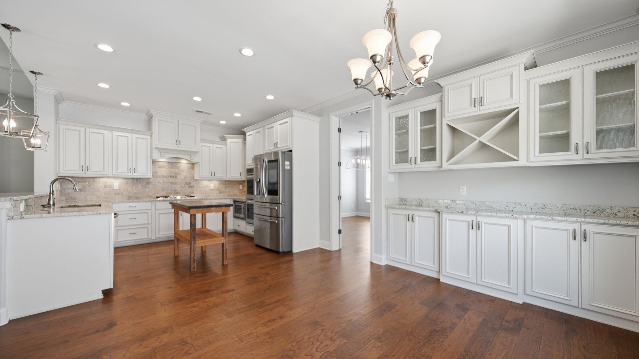 1058 Shanborne Cove Collierville, TN 38017 - Photo 13 of 39 Kitchen featuring hanging lights, white cabinetry, light stone counters, glass fronted cabinets, and dark wood-style floors