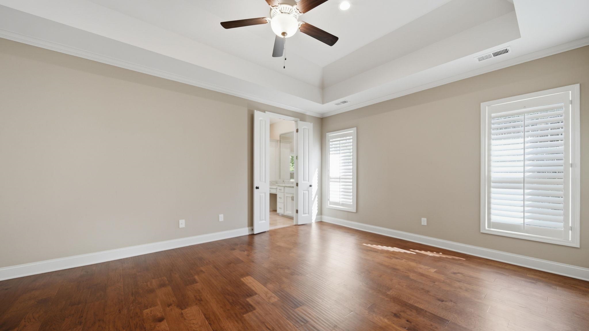 1058 Shanborne Cove Collierville, TN 38017 - Photo 19 of 39 Unfurnished bedroom featuring dark wood-type flooring, connected bathroom, a ceiling fan, a raised ceiling, and crown molding