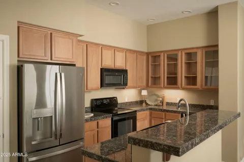 a kitchen with stainless steel appliances granite countertop a refrigerator a stove top oven and a sink with wooden floor