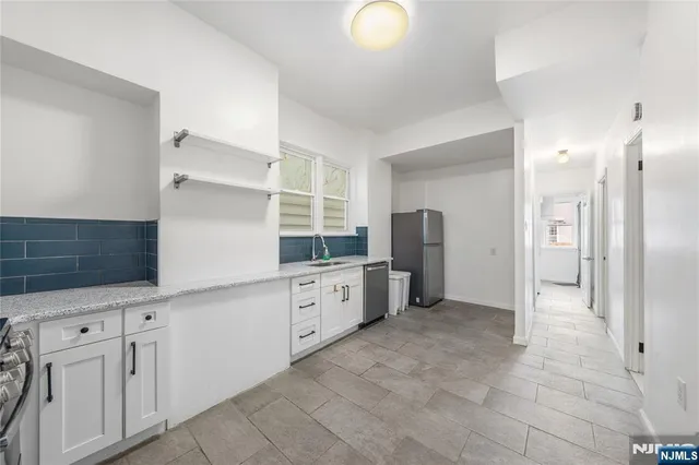 a large white kitchen with granite countertop a refrigerator and white cabinets