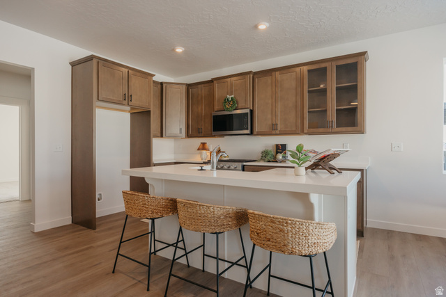 4595 North Fallow Way, Unit 511 Eagle Mountain, UT 84005 - Photo 12 of 32 Kitchen featuring a kitchen bar, stainless steel microwave, light wood-style flooring, glass fronted cabinets, and a center island with sink