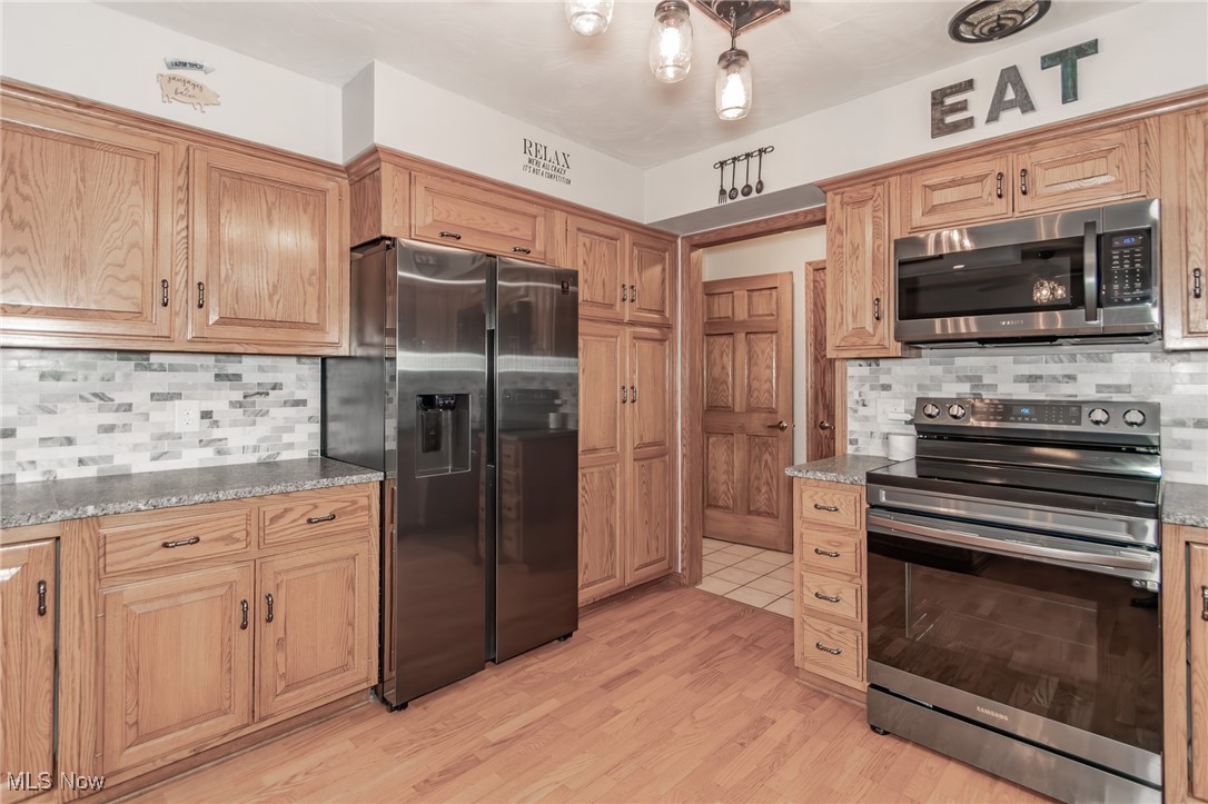 2866 South County Line Road Madison, OH 44057 - Photo 25 of 48 Kitchen featuring decorative backsplash, visible vents, stainless steel appliances, stone countertops, and light wood-style floors