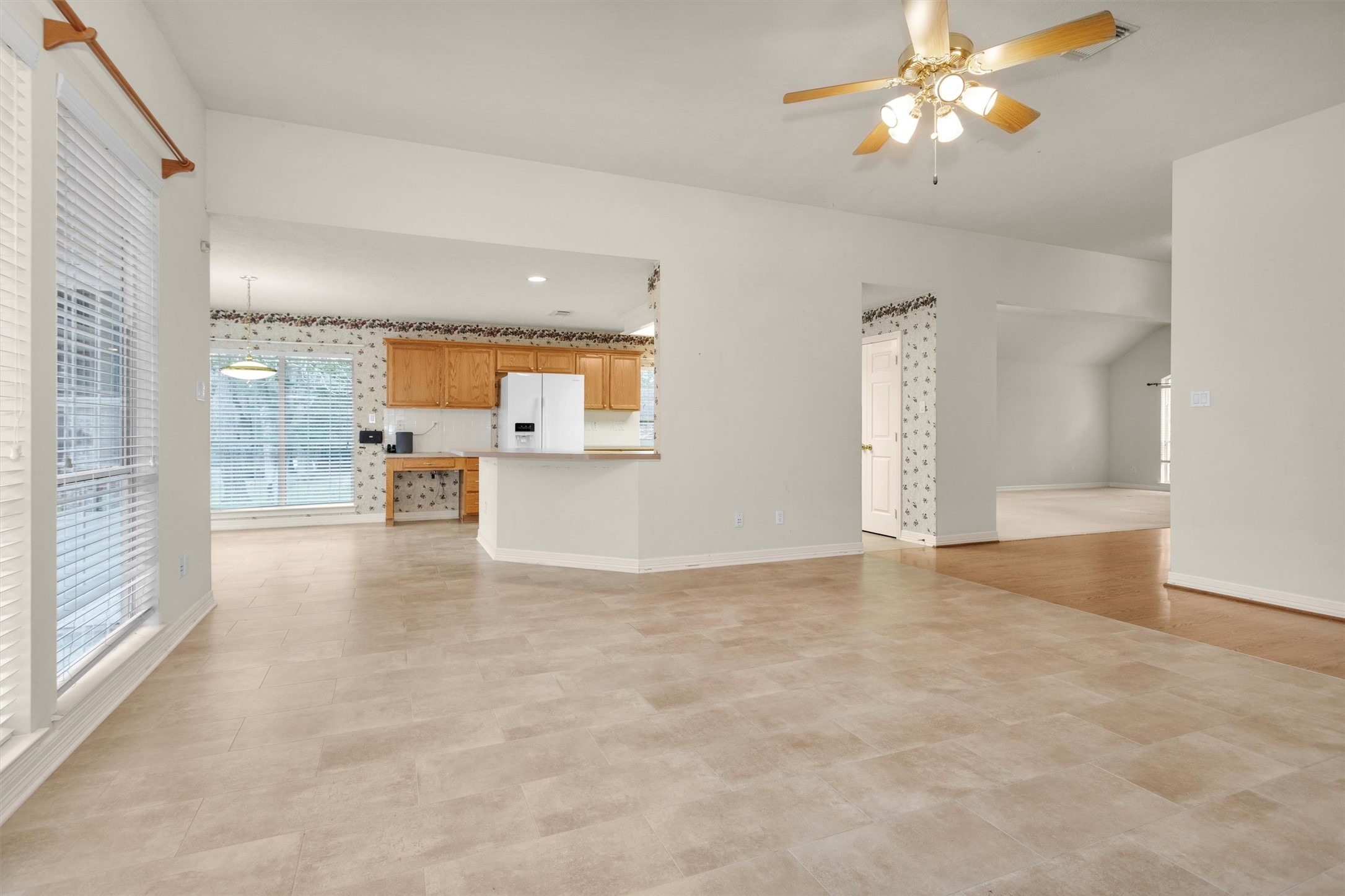 2419 Carriage Ridge Lane Conroe, TX 77384 - Photo 15 of 39 This spacious, open-concept living area features tile flooring, a ceiling fan, and ample natural light. The kitchen, visible in the background, has wooden cabinets and white appliances. Large windows enhance the room's brightness.