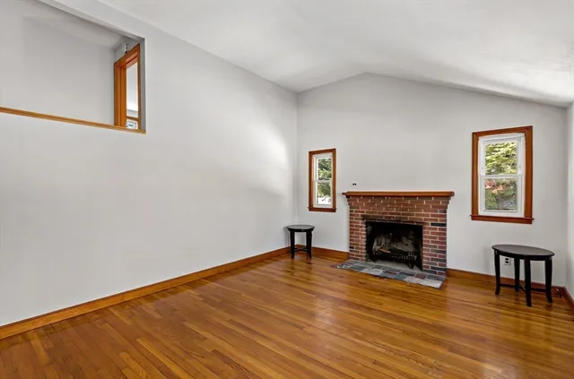 a view of an empty room with wooden floor fireplace and a window