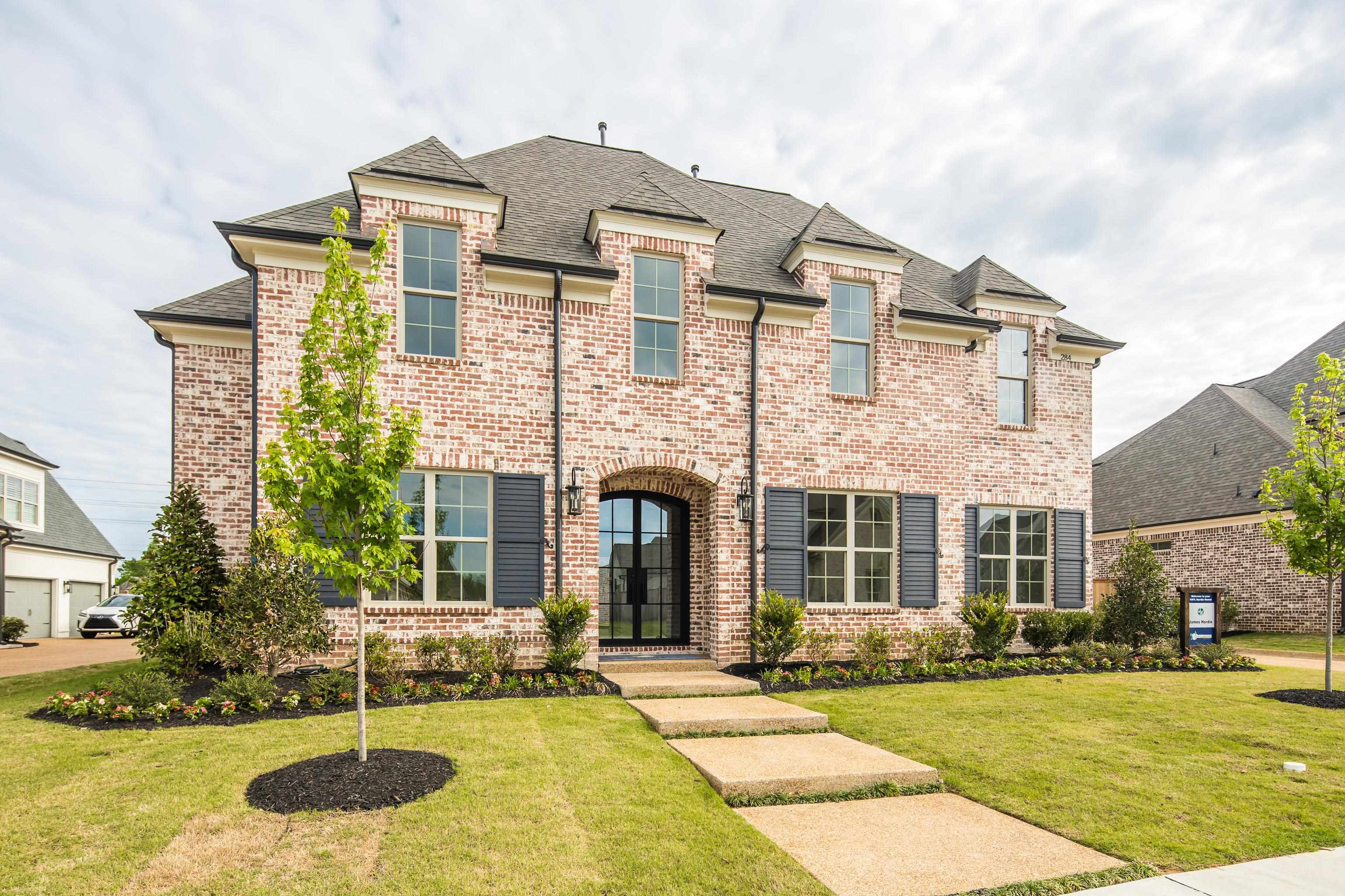 284 Keisie Lane Collierville, TN 38017 - Photo 1 of 34 Brick facade residence featuring arched entry door, dark shutters, multiple dormer windows, a concrete walkway, and landscaped front yard