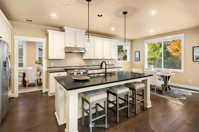 a kitchen with stainless steel appliances granite countertop a stove a sink dishwasher a refrigerator and a dining table with wooden floor