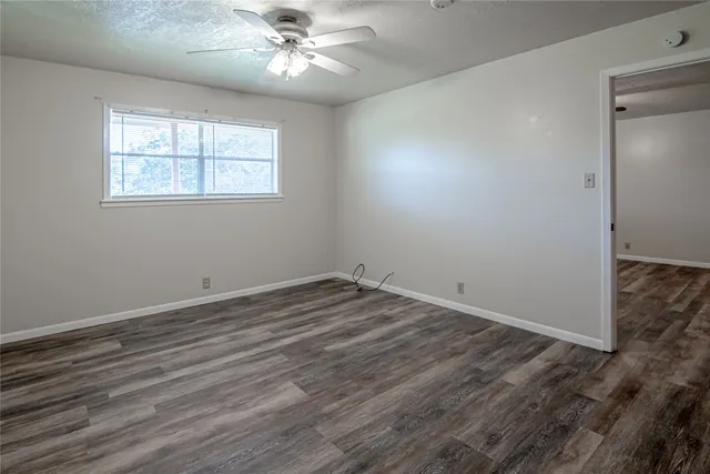 an empty room with wooden floor chandelier fan and windows