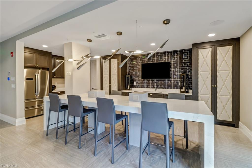 1135 3rd Avenue South, Unit 403 Naples, FL 34102 - Photo 28 of 34 Kitchen with hanging light fixtures, freestanding refrigerator, a large island, dark wood finish cabinets, and light stone counters