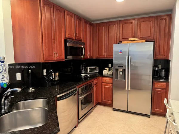 a kitchen with stainless steel appliances granite countertop a refrigerator a stove and a sink with wooden cabinets