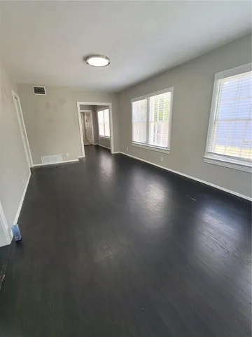 an empty room with wooden floor and windows with curtains