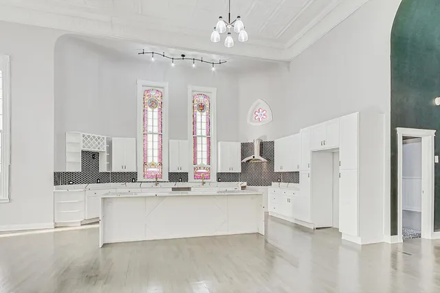 a large white kitchen with kitchen island a chandelier and a view of living room