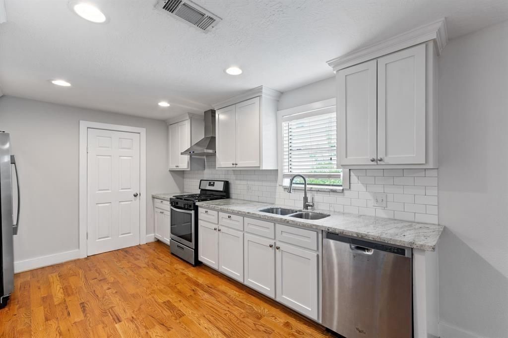 1305 Idylwild Street Houston, TX 77009 - Photo 9 of 31 Modern kitchen with stainless steel appliances, white cabinetry, and a subway tile backsplash. Hardwood floors add warmth, and ample natural light brightens the space.
