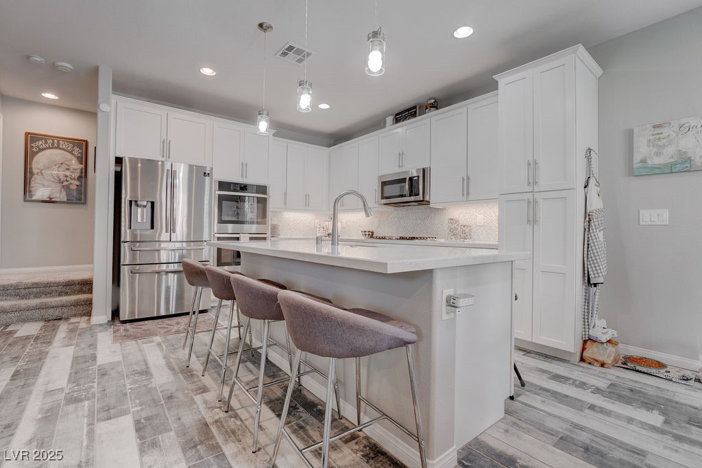 8099 Rams Collide Street Las Vegas, NV 89166 - Photo 2 of 72 Kitchen featuring stainless steel appliances, a center island with sink, pendant lighting, backsplash, and light wood finished floors