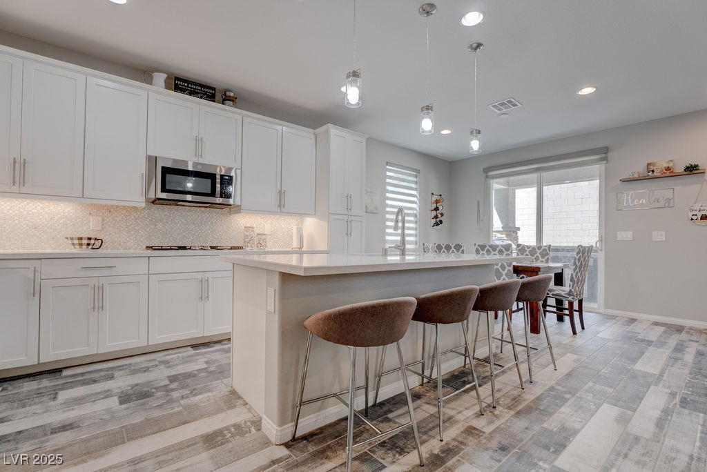 8099 Rams Collide Street Las Vegas, NV 89166 - Photo 10 of 72 Kitchen with decorative light fixtures, tasteful backsplash, light wood-style floors, recessed lighting, and white cabinetry