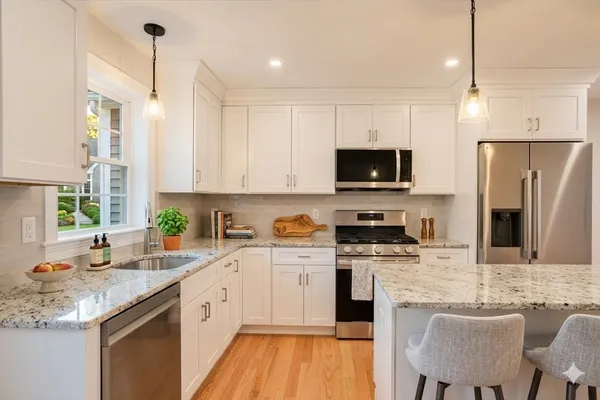 a kitchen with stainless steel appliances granite countertop a stove top oven a sink dishwasher a refrigerator and a dining table with wooden floor