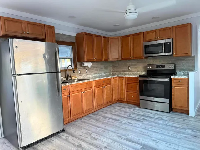 a kitchen with stainless steel appliances granite countertop a refrigerator a stove top oven a sink and dishwasher with wooden floor