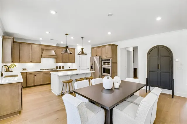 a kitchen with stainless steel appliances kitchen island granite countertop a dining table chairs and a refrigerator