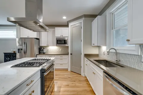 a kitchen with stainless steel appliances granite countertop a sink stove a refrigerator and white cabinets with wooden floor