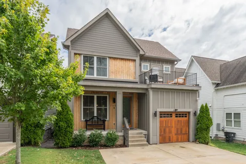 a view of a white house with a small yard plants and large tree