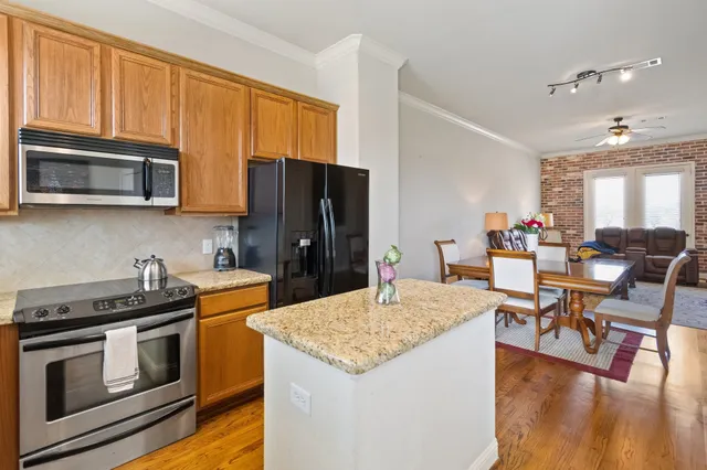 a kitchen with stainless steel appliances kitchen island granite countertop a refrigerator a stove top oven a sink dishwasher and white cabinets with wooden floor