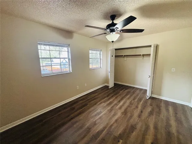 an empty room with wooden floor fan and windows