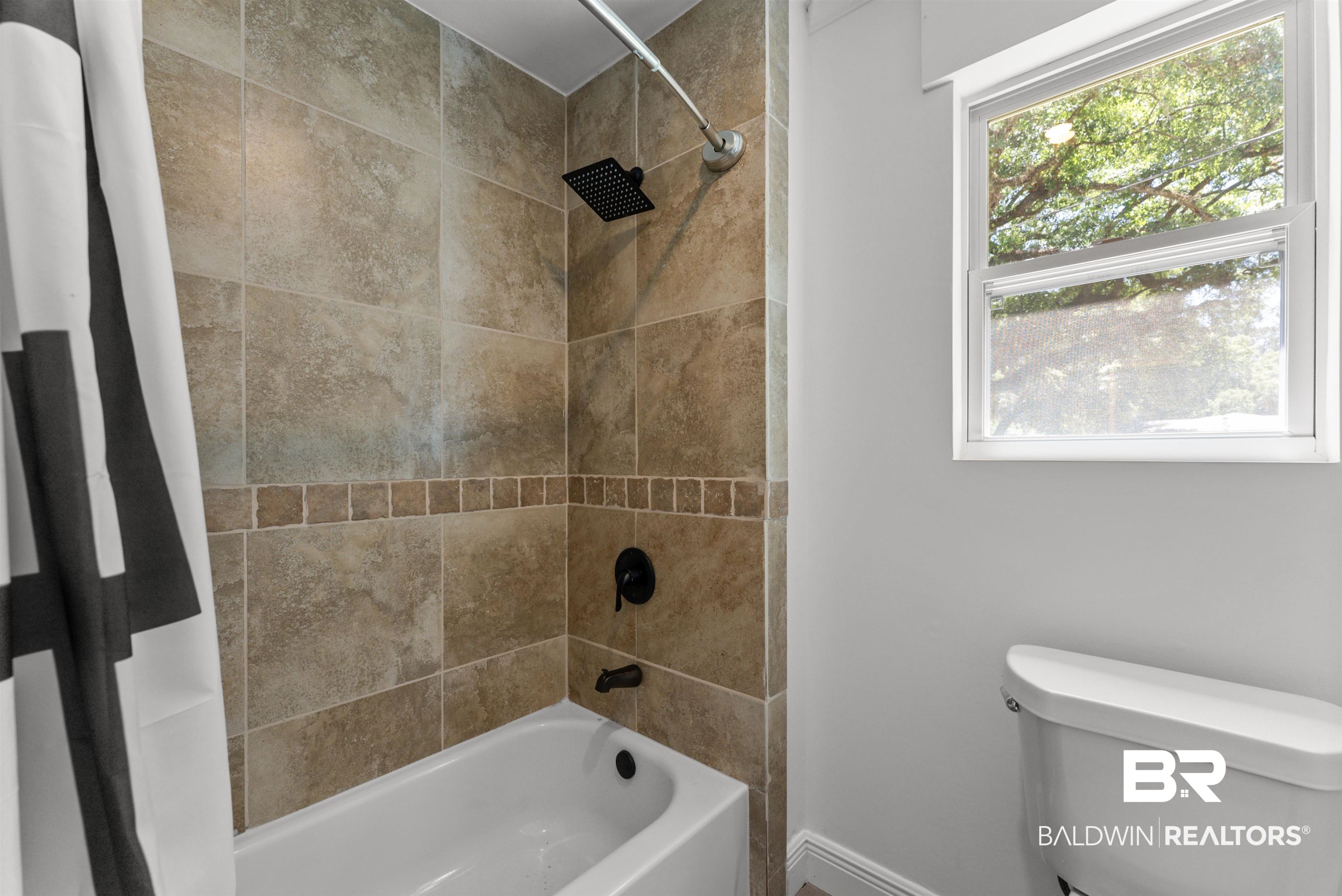 6447 Bemis Lane Bon Secour, AL 36511 - Photo 53 of 62 Bathtub with tiled surround featuring a decorative border, matte black shower fixtures, and a window with white trim