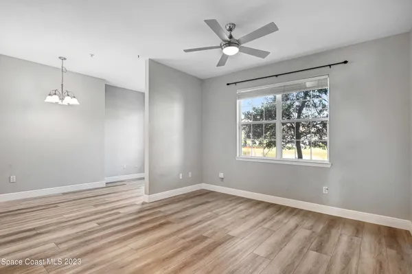 an empty room with wooden floor chandelier fan and windows