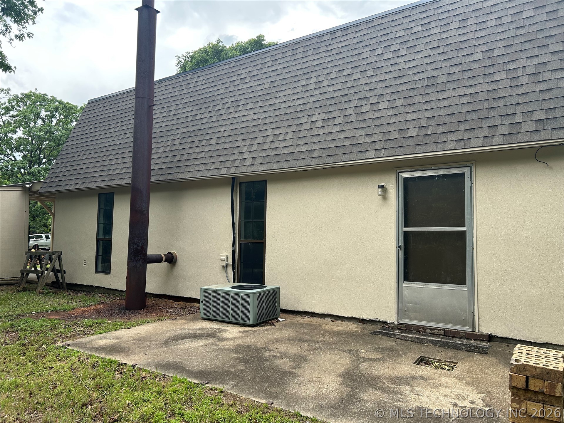 Rear exterior featuring a concrete patio, light-colored stucco siding, and a gray shingle roof