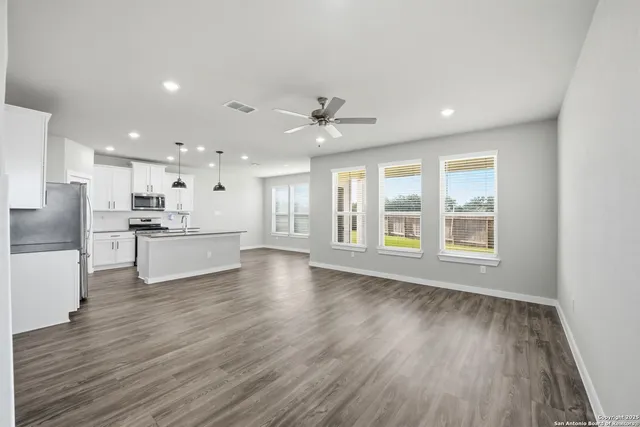 a view of an empty room with wooden floor and a kitchen