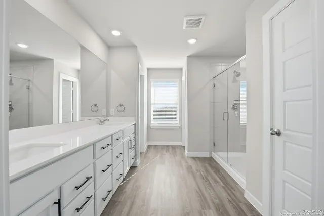 a bathroom with a granite countertop double vanity sink a mirror and a shower