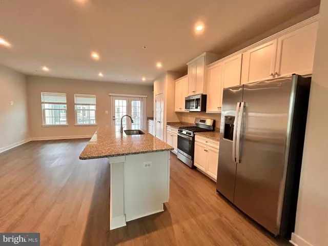 a kitchen with stainless steel appliances granite countertop a refrigerator a sink dishwasher a stove and white countertops with wooden floor