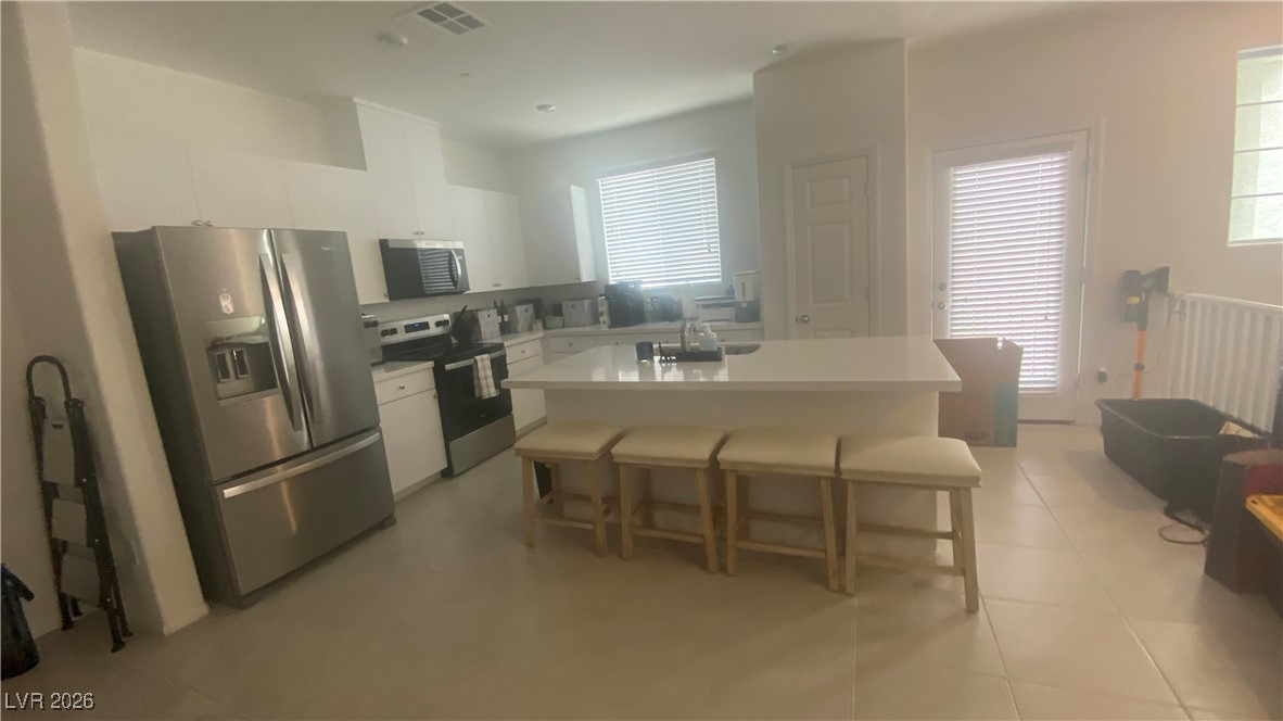 5675 Spellbinding Street Las Vegas, NV 89148 - Photo 13 of 18 Kitchen featuring appliances with stainless steel finishes, white cabinetry, a center island with sink, and a kitchen breakfast bar