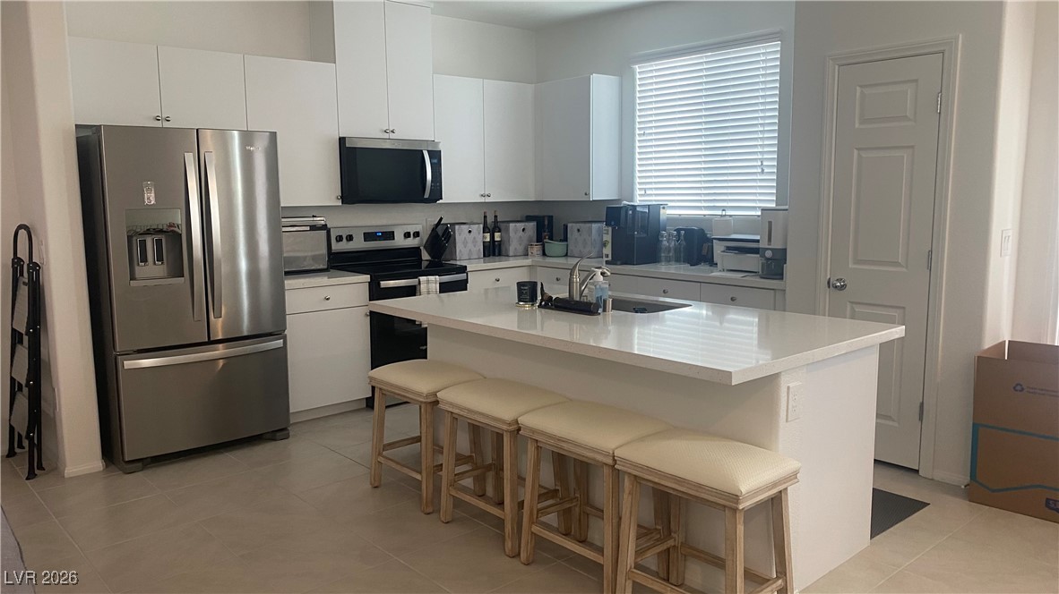 5675 Spellbinding Street Las Vegas, NV 89148 - Photo 3 of 18 Kitchen featuring appliances with stainless steel finishes, a kitchen bar, a center island with sink, white cabinetry, and light stone counters