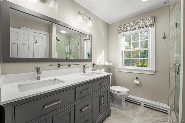 a bathroom with a toilet a sink a mirror a window and vanity