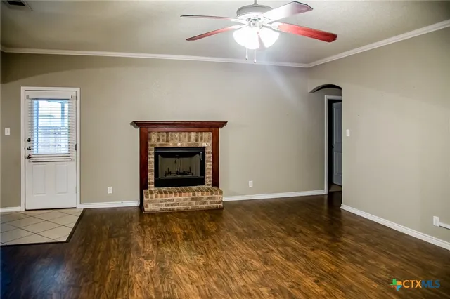 an empty room with wooden floor a ceiling fan and fireplace
