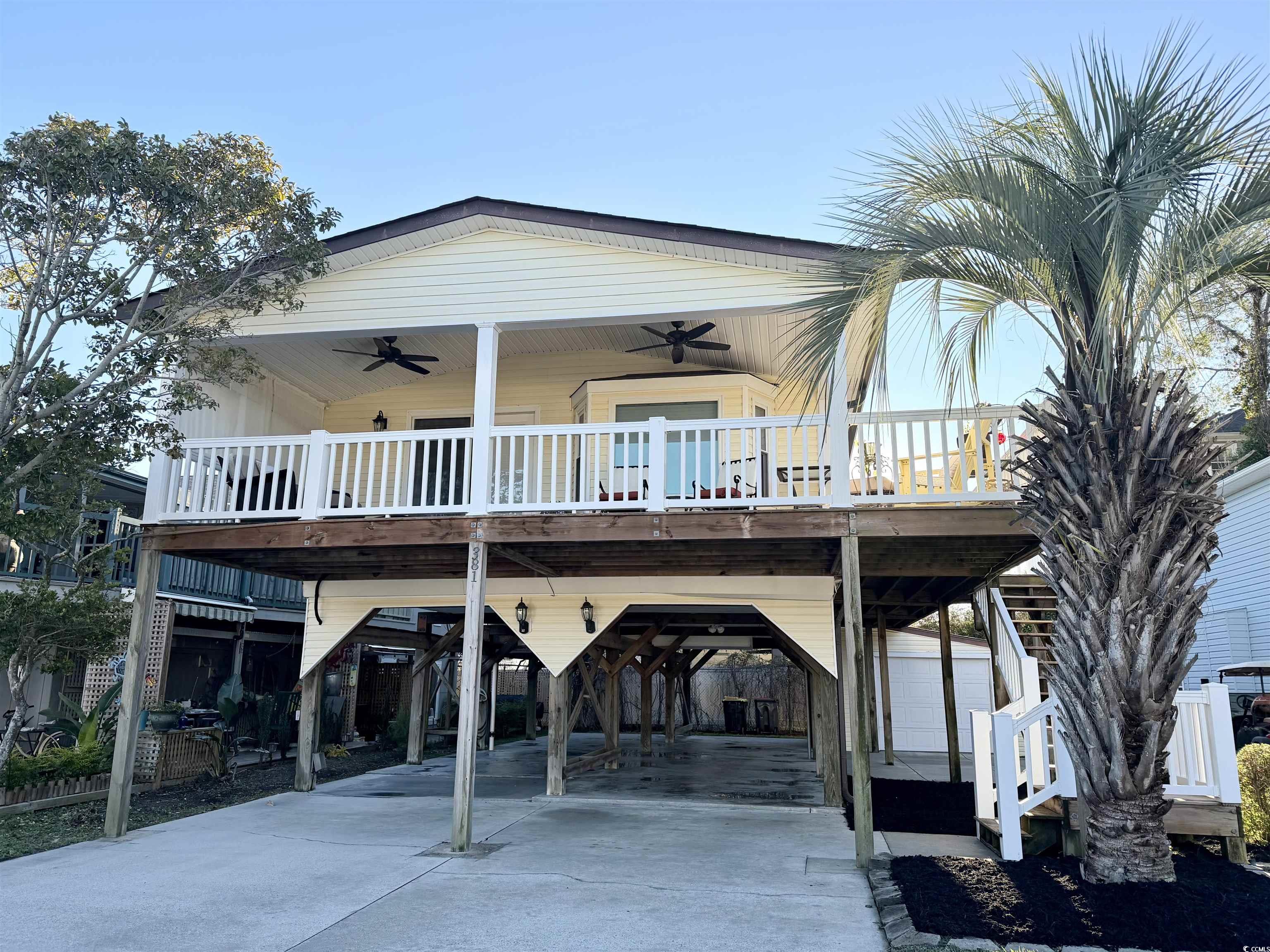 View of front of house with a carport, ceiling fan, driveway, a wooden deck, and a patio