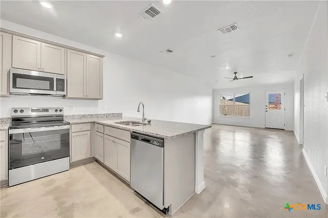 a kitchen with stainless steel appliances granite countertop a stove top oven a sink dishwasher and a refrigerator with wooden floor