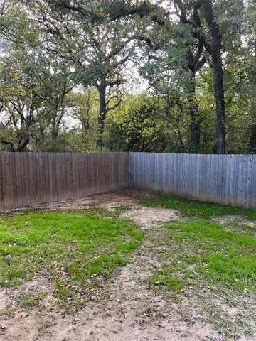 a view of a backyard with large trees and wooden fence