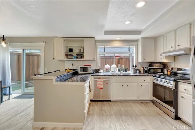 a kitchen with stainless steel appliances granite countertop a stove top oven a sink a refrigerator and white cabinets with wooden floor