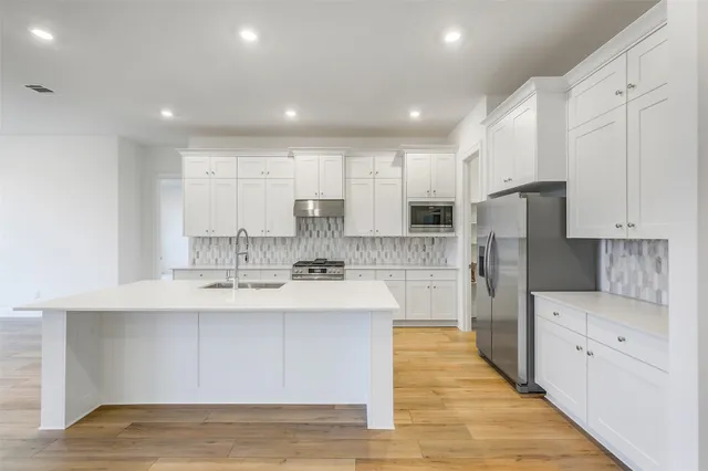 a large kitchen with stainless steel appliances kitchen island granite countertop a stove a sink and white cabinets