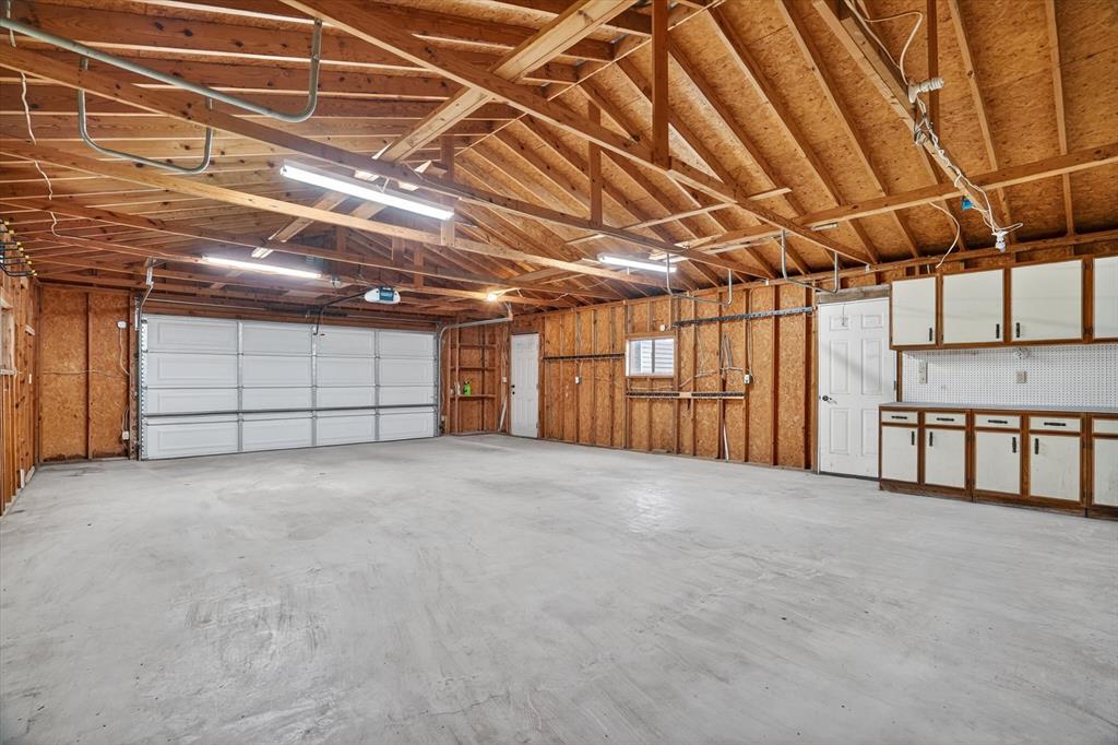 7757 Berry Road Burleson, TX 76028 - Photo 26 of 36 Spacious garage featuring a concrete floor, exposed wood ceiling beams, a white paneled garage door, and built-in cabinetry with a tiled backsplash