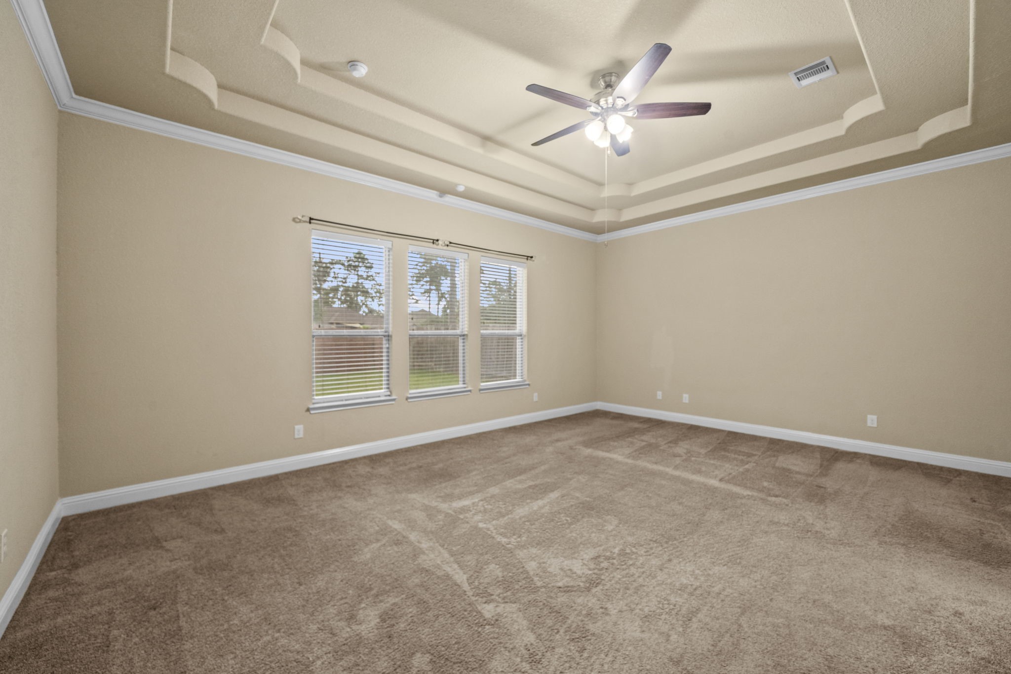 14215 Spindle Arbor Road Cypress, TX 77429 - Photo 30 of 47 Spacious room with beige walls and carpet, featuring a tray ceiling with a ceiling fan. Large windows provide natural light and a view of the backyard.