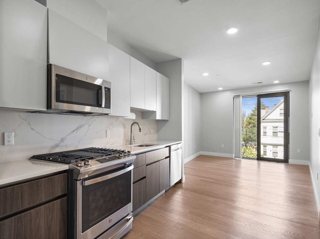 9 Central Street, Unit 207 Somerville, MA 02143 - Photo 5 of 32 a kitchen with stainless steel appliances granite countertop a stove a sink and a microwave