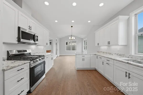 a large kitchen with stainless steel appliances granite countertop a stove a sink dishwasher and a microwave oven with white cabinets