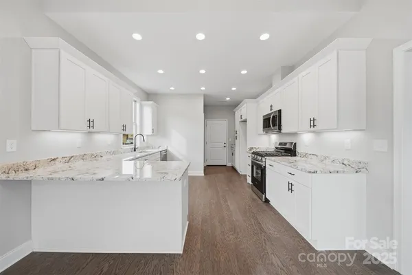 a kitchen with stainless steel appliances kitchen island granite countertop a stove a sink a refrigerator and white cabinets with wooden floor