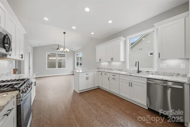 a large white kitchen with stainless steel appliances granite countertop a stove and a sink