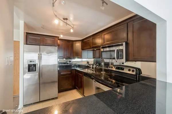 a kitchen with stainless steel appliances kitchen island granite countertop a refrigerator a stove and a sink with wooden floor