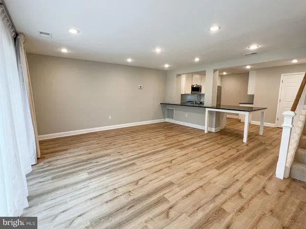 an empty room with wooden floor and way to kitchen